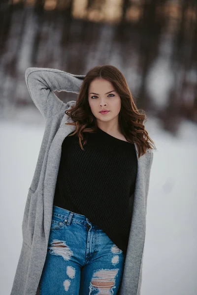雪に覆われた冬の公園に黒いシャツ ジーンズ ジャケットを着た若い白人女性 — ストック写真