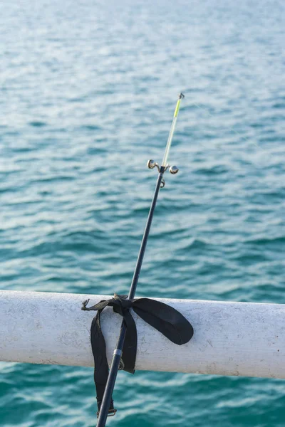 A vertical shot of a fishing rod knotted with black cloth on pier metal bar