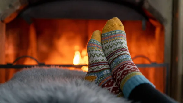A woman\'s legs in woolen socks heat up near a cozy fireplace