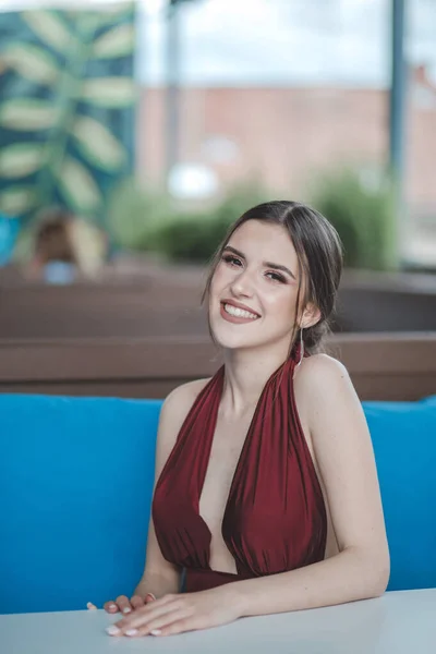 一个白人微笑的女人在户外咖啡馆里穿着红色性感晚礼服的纵向照片 — 图库照片