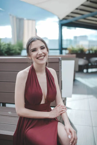 一个白人微笑的女人在户外咖啡馆里穿着红色性感晚礼服的纵向照片 — 图库照片