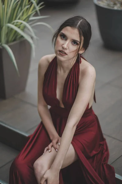 一个穿着红色性感晚礼服的优雅女人坐在户外咖啡馆楼梯上的垂直照片 — 图库照片