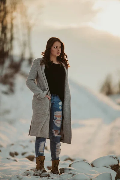 雪に覆われた森の中でコートとセーターを着たジーンズを身に着けている大人のブルネットの女性の浅い焦点 — ストック写真