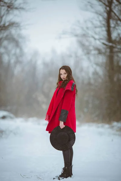 雪の森でスタイリッシュな赤いコートを身に着けている若いブルネットの女の子のフルボディショット — ストック写真