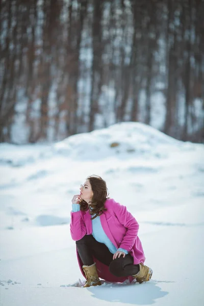 Молодая Задумчивая Брюнетка Очках Преклонила Колени Снежном Лесу Розовом Пальто — стоковое фото