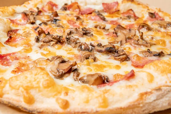 A closeup of ham and mushroom pizza on a box