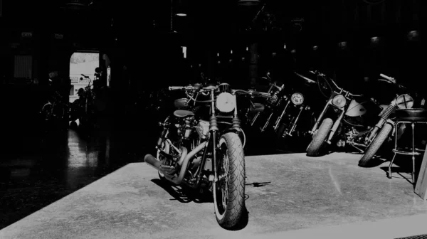 老式摩托车在只有横向灯光照明的车库黑暗中排成一排 在底部 一个敞开的门 — 图库照片