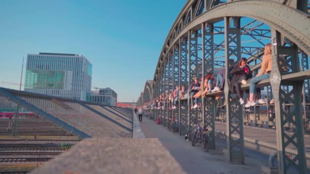 多くの人が太陽の下でハッカーの橋に座っています 橋はミュンヘンの街の景色を眺めながら仕事の後のビールのための人気のミーティングポイントです — ストック動画