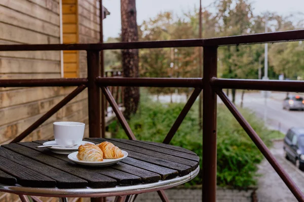 バルコニーの木製テーブルの上で朝のカプチーノとクロワッサンのクローズアップショット — ストック写真