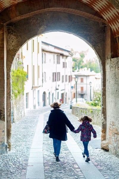 一个高加索女人牵着女儿的手穿过狭窄的拱形小巷的倒影 — 图库照片