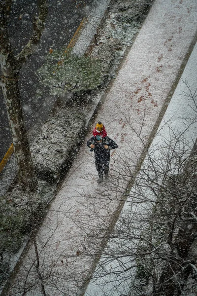 Wysokie Ujęcie Nierozpoznawalnego Mężczyzny Niosącego Dziecko Ramionach Gdy Pada Śnieg — Zdjęcie stockowe