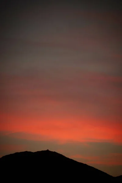 山のシルエットを通して見られる燃えるような赤い夕日の垂直ショット 壁紙に最適です — ストック写真