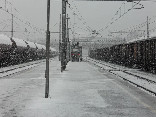 悲観的な日に大雪の下で複数の鉄道線路や貨物列車がある鉄道駅 — ストック写真