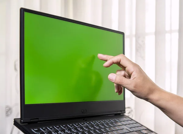 A closeup of a laptop with green screen space and a person\'s fingers tapping on the screen