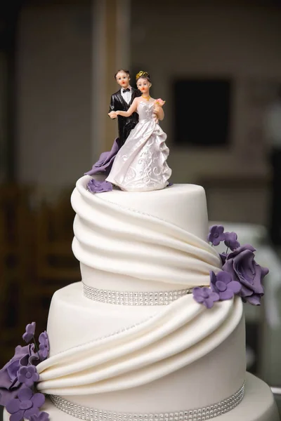 A vertical shot of decorative wedding cake with purple candy flowers and cake topper