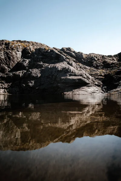 日の出時に鏡のような海に反射した天然の荒波岩崖の垂直ショット — ストック写真