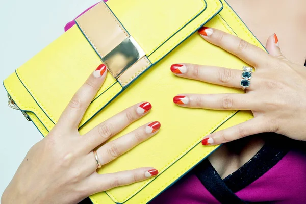 A closeup shot of female hands with nail polish holding a yellow purse