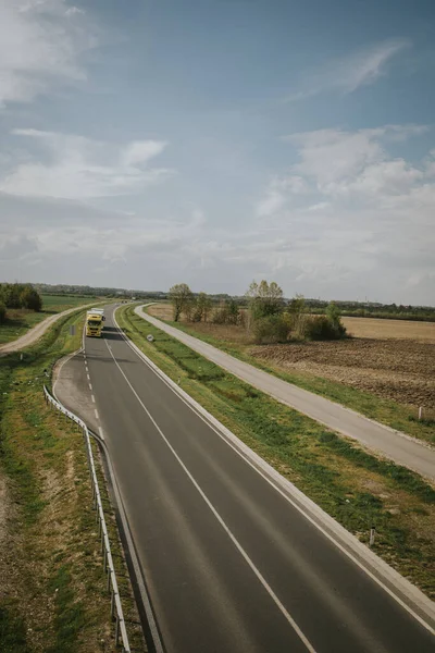 Samotna Żółta Ciężarówka Podróżująca Długiej Pustej Drodze Otoczona Polami Trawy — Zdjęcie stockowe