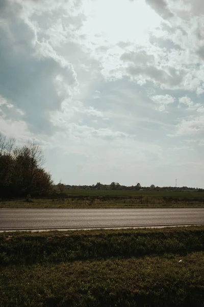 Вертикальный Снимок Пустой Дороги Бегущей Вдоль Травянистого Поля Ярким Облачным — стоковое фото