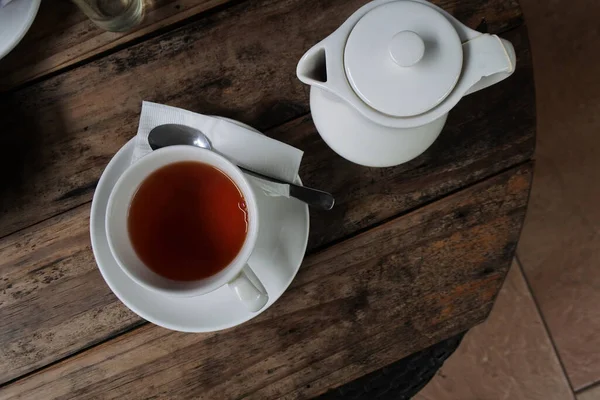 ティーポット付きの木製テーブルの上にナプキンとスプーンでソーサーにお茶のカップのトップビュー — ストック写真