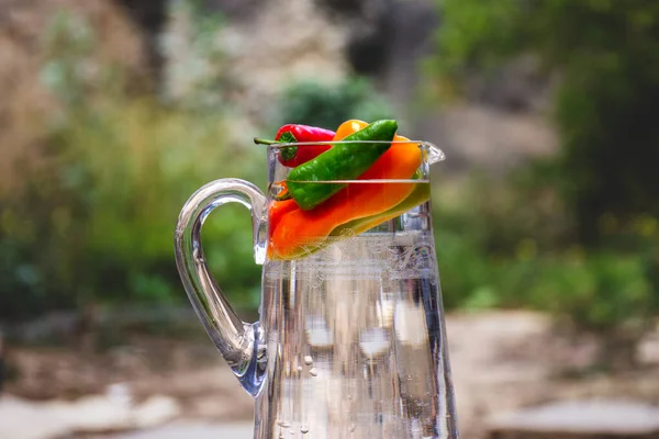 Closeup Glass Jug Water Colorful Peppers Outdoors Trees Blurred Background — Stock Photo, Image