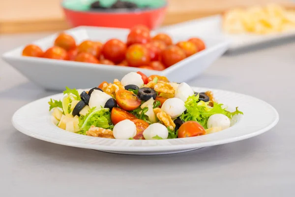 A serving of Mediterranean diet salad Santorini with mozzarella, walnuts, cherry tomato, apple, assorted lettuce, black olives, olive oil
