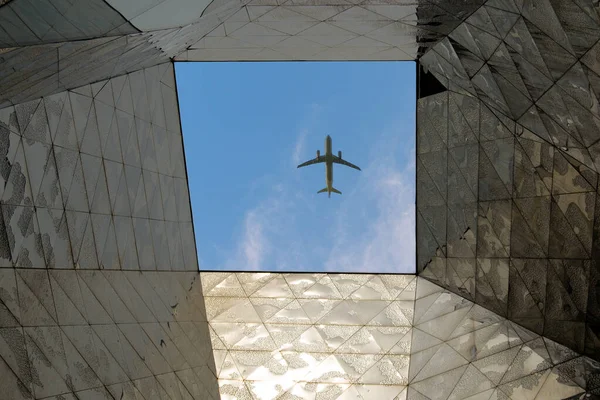ビルの屋根の穴を通って地面から見た晴れた日の青い空を飛ぶ飛行機 — ストック写真