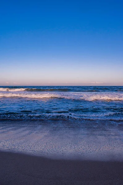 A vertical shot of the beach under a clear sky in the evening