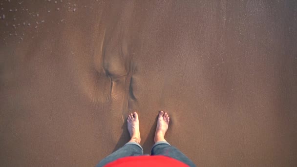 突然足を濡らす小さな波で砂浜に立っている男のトップビュー — ストック動画