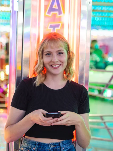 一个年轻的金发女子在游乐园用手机的垂直照片 — 图库照片