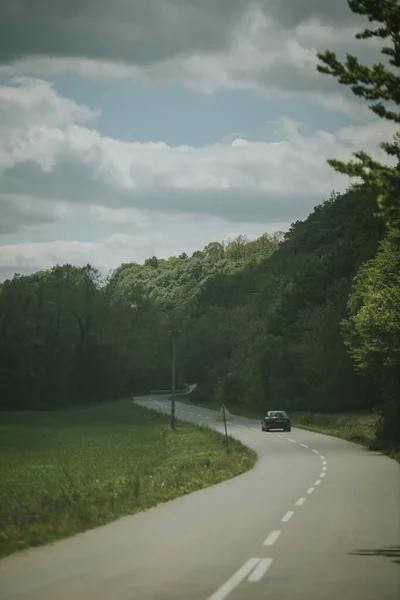 Jediné Černé Auto Jedoucí Klikaté Cestě Vysokými Zelenými Stromy Travnatým — Stock fotografie