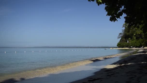 Bred bild av en liten holme på kroppen av havet i fjärran under en klarblå himmel — Stockvideo