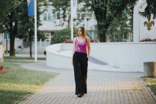 若いですブロンド女性モデルポーズオンザ歩道でピンクのブラウスと黒のパンツ — ストック写真