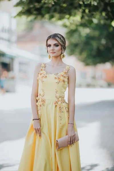 一个年轻的金发女郎穿着黄色的花朵晚礼服摆姿势的垂直照片 — 图库照片