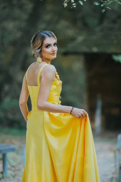 一个年轻的金发女郎穿着黄色的花朵晚礼服摆姿势的垂直照片 — 图库照片