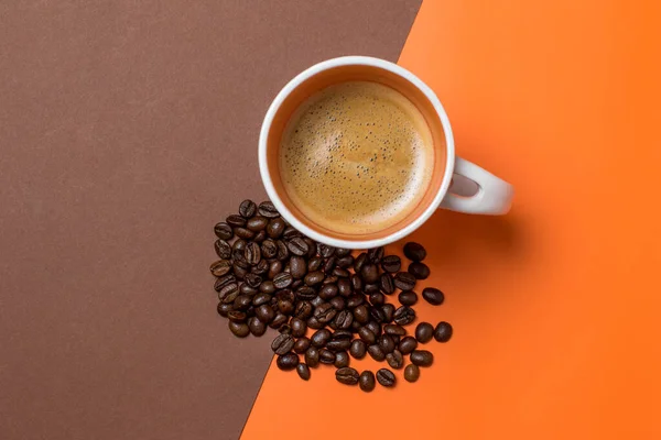 coffee in a white coffee cup and many coffee beans placed in a brown and orange background