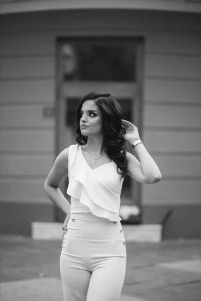 一个年轻的黑发卷曲女模特儿穿着典雅的白色衬衫摆姿势的灰白色照片 — 图库照片