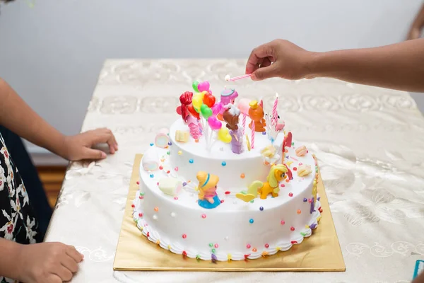 漫画のキャラクターとカラフルな誕生日ケーキのろうそくを燃やす手のクローズアップショット — ストック写真