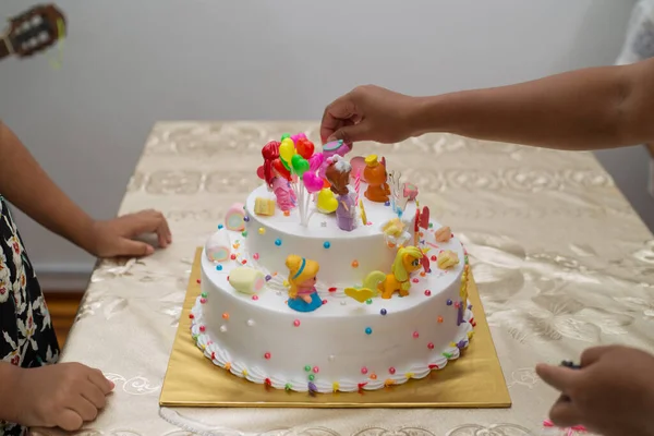 漫画のキャラクターとカラフルな誕生日ケーキのキャンドルを燃やす手のクローズアップショット — ストック写真