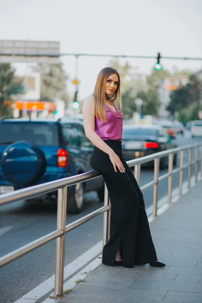 一位漂亮的白人女性 穿着时髦的紫色和黑色衣服 靠着街边的栅栏 — 图库照片