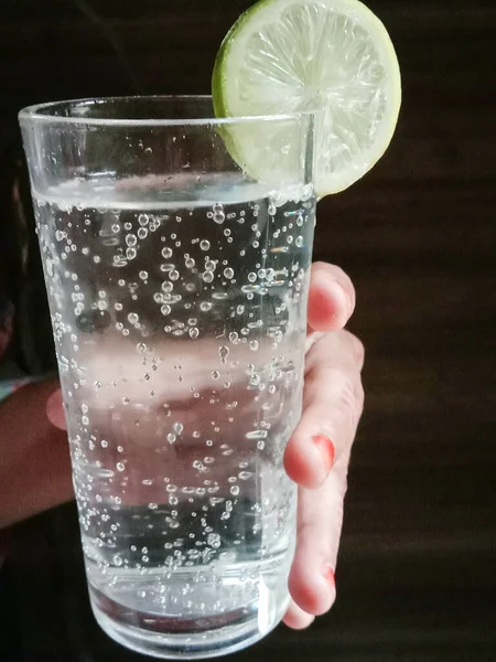 Zbliżenie Ręki Trzymającej Szklankę Przezroczystego Napoju Bezalkoholowego Plasterkami Cytryny — Zdjęcie stockowe