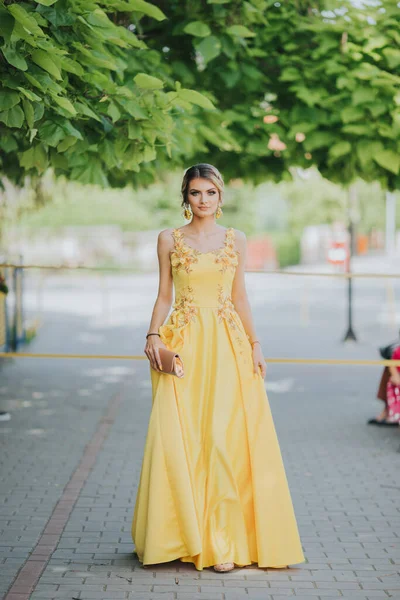 一个美丽的白种人金发女子在街上举着典雅的黄色连衣裙的垂直画像 — 图库照片
