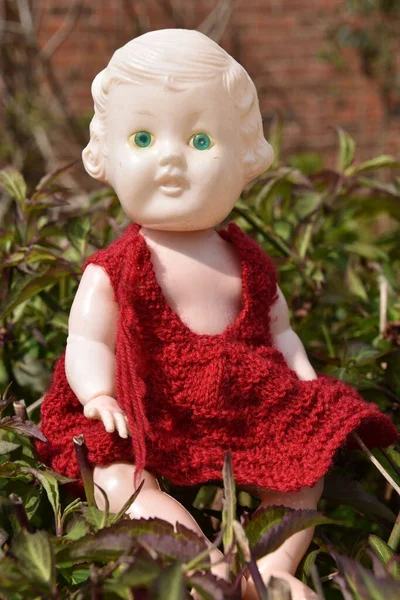 一个穿着红色衣服坐在草地上的毛骨悚然的老娃娃的垂直镜头 — 图库照片