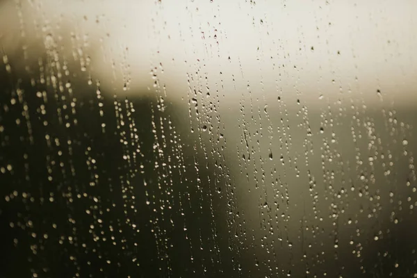 雨滴と薄暗い背景で覆われたガラス窓のぼやけたショット — ストック写真