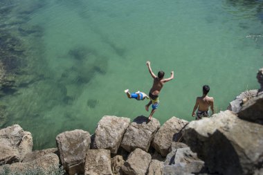 A group of young boys jumping into the sea from a small cliff, Cascais. Portugal clipart