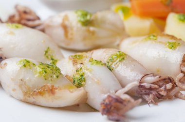 A closeup of boiled squids with green sauce, boiled potatoes, and carrots on a pla clipart