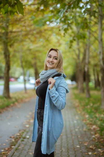 一名身穿蓝色夹克并在波斯尼亚和黑塞哥维那公园摆姿势的金发年轻女子的肤浅镜头 — 图库照片