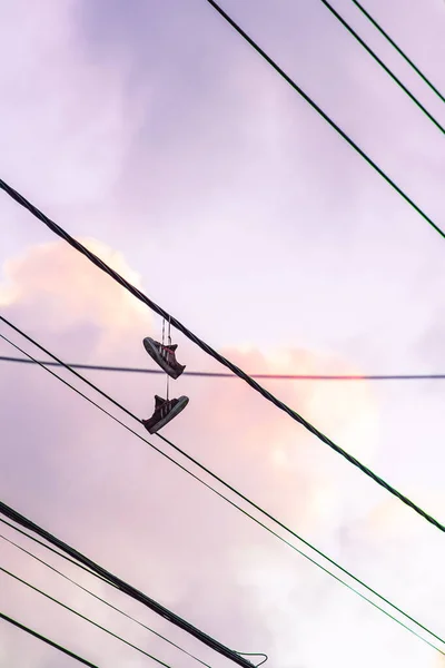 在紫色色调的天空背景上挂在街道铁丝网上的鞋子的艺术照片 — 图库照片