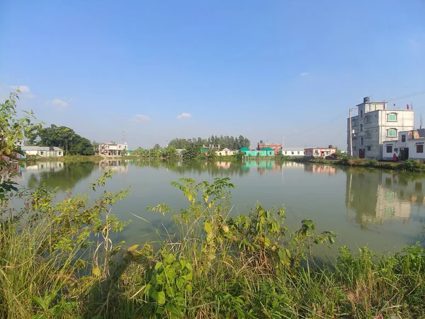 一个适合钓鱼的池塘的照片 上面覆盖着绿色的植物 周围环绕着一些小建筑物 — 图库照片
