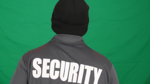 Hdの緑の壁に黒いボンネットを身に着けている男性のセキュリティ担当者を歩くのバックビュー — ストック動画